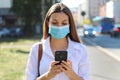 COVID-19 Pandemic Coronavirus Young Woman Wearing Surgical Mask Using Smart Phone App in City Street to Aid Contact Tracing