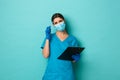 Covid-19, pandemic and medicine concept. Close-up of puzzled female doctor in medical mask, gloves and scrubs, holding