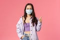 Covid19, quarantine, people concept. Happy confident young girl show thumbs-up while standing in medical face mask and