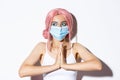 Covid-19, social distancing and people concept. Close-up of cute party girl in pink wig and medical mask, holding hands