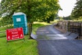 A Covid-19 social distancing warning sign and a plastic portable toilet next to a cattle grid on a public footpath at an outdoor Royalty Free Stock Photo