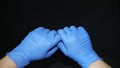 COVID-19 Two hands covered in blue surgical gloves, holding by thumb and forefinger, on black background