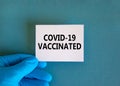 Covid-19 vaccinated symbol. Hand in blue glove with white card. Concept words 'Covid-19 vaccinated'.