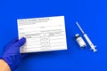 COVID-19 vaccination record card in doctor`s hand, immunization concept, blue table with syringe and vaccine vial Royalty Free Stock Photo
