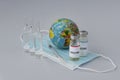 Covid vaccine, syringe for injection and toy globe on medical maski on light background,