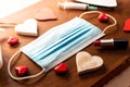 Covid valentine`s day hygiene concept. face mask with red hearts on wooden background. top view of hand sanitizer and lipstick an Royalty Free Stock Photo