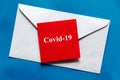 COVID-19 word written on red note pad on top of white envelope on blue background. Royalty Free Stock Photo
