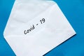 Covid-19 word written on white color envelope on blue background.