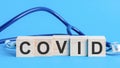 Covid word written on wooden blocks and stethoscope on light blue background
