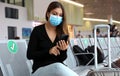 COVID-19 Young tourist woman with surgical mask using phone and sitting respecting social distancing at the airport Royalty Free Stock Photo