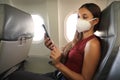 COVID-19 Young woman on airplane wearing KN95 FFP2 protective mask reading information on mobile phone during coronavirus pandemic