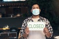 Covids making things a little tough. a young man standing outside his restaurant and wearing a face mask while holding a