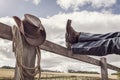 Cowboy boots and hat with feet up on fence resting with legs crossed