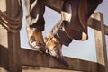 Cowboy boots and hat sitting on fence at rodeo stables with feet up resting Royalty Free Stock Photo