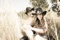 Cowboy and cowgirl couple sitting in grass, laughing as they tickle each other. Royalty Free Stock Photo