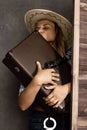 Cowboy girl or pretty woman in stylish hat and blue plaid shirt holding gun and old suitcase Royalty Free Stock Photo