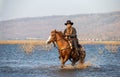 Cowboy on his horse walking through dust in the lake