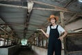 cowboy woman posing with hands carrying something while wearing a hat in a large cow stable