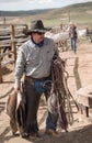 Cowboy wrangler carrying his hackamore, horse blanket, lead rope and saddle to tack room