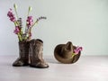 Cowgirl or cowboy brown hat with cowgirl or cowboy brown leather boots with one boot filled with pink and purple artificial