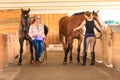 Cowgirl and jockey walking with horses in stable