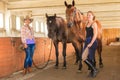 Cowgirl and jockey walking with horses in stable Royalty Free Stock Photo