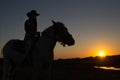 A cowgirl riding a horse on a ranch is silhouetted against the afternoon sun. Royalty Free Stock Photo