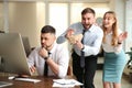 Coworkers popping paper bag behind their colleague in office. Funny joke