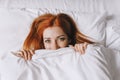 coy young woman hiding under bed cover