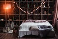 Coziness, comfort, interior and holidays concept - cozy bedroom with bed and garland lights at home. A rack with books Royalty Free Stock Photo