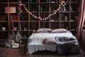 Coziness, comfort, interior and holidays concept - cozy bedroom with bed and garland lights at home. A rack with books Royalty Free Stock Photo