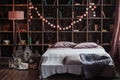 Coziness, comfort, interior and holidays concept - cozy bedroom with bed and garland lights at home. A rack with books Royalty Free Stock Photo