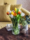 Cozy apartment interior-a bouquet of tulips in a vase, books on a wooden table on the background of a yellow sofa Royalty Free Stock Photo