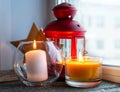 Cozy atmosphere - candles on a wooden window sill at dusk. Candles in glass candlesticks and a red lantern candlestick Royalty Free Stock Photo