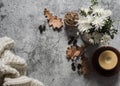 Cozy autumn background. Candle, autumn flowers, knitted blanket, dry leaves on a gray background, top view