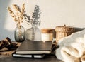 Cozy autumn home still life of dry flowers in vase, straw box, glass candle, knitted blanket and black notepads on a rustic wooden Royalty Free Stock Photo