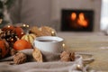 Cozy autumn. Warm cup of tea, pumpkins, autumn leaves, cones, cozy scarf and lights on rustic wooden table in farmhouse. Fall in