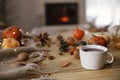Cozy autumn. Warm cup of tea, pumpkins, autumn leaves, cones, cozy scarf and lights on rustic wooden table in farmhouse. Fall in