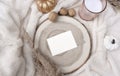 Cozy autumn or winter layout still life. Mockup invitation card, candles, pumpkins wooden tray on white blanket.