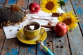 Cozy autumn: a yellow cup with coffee beans against the background of sunflower flowers, red apples, eyeglasses, close-up Royalty Free Stock Photo