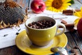 Cozy autumn: a yellow cup with coffee beans close-up on a background of sunflower flowers and red apples Royalty Free Stock Photo