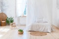 Cozy bedroom in light colors with a wooden floor, a large four-poster bed, wicker chair and basket of flowers. Scandinavian simpli Royalty Free Stock Photo