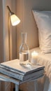 Cozy bedside table with modern lamp, stack of books, glass carafe, and candle Royalty Free Stock Photo