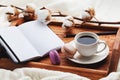 Cozy breakfast with cup of coffee, cotton flower, macaroon and open notebook on rustic wooden tray in bed. Royalty Free Stock Photo