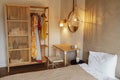 Cozy bright interior of a bedroom with a wooden wardrobe and clothes, a table, a chair and a bed