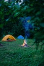 Cozy camping, lifestyle and adventure concept. Warm campfire and two rent in serene summer spruce forest setting. Bonfire from old