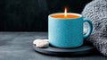 A cozy candle in a blue mug placed beside a soft knit blanket and a cookie Royalty Free Stock Photo