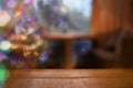 Cozy Christmas blurred background with bokeh, table, Christmas tree in living room and wooden tabletop in foreground. Royalty Free Stock Photo