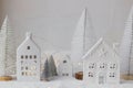 Cozy christmas miniature village. Stylish little ceramic houses and trees on snow blanket with golden lights on white background. Royalty Free Stock Photo