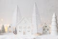 Cozy christmas miniature village. Stylish little ceramic houses and trees on snow blanket with golden lights on white background. Royalty Free Stock Photo